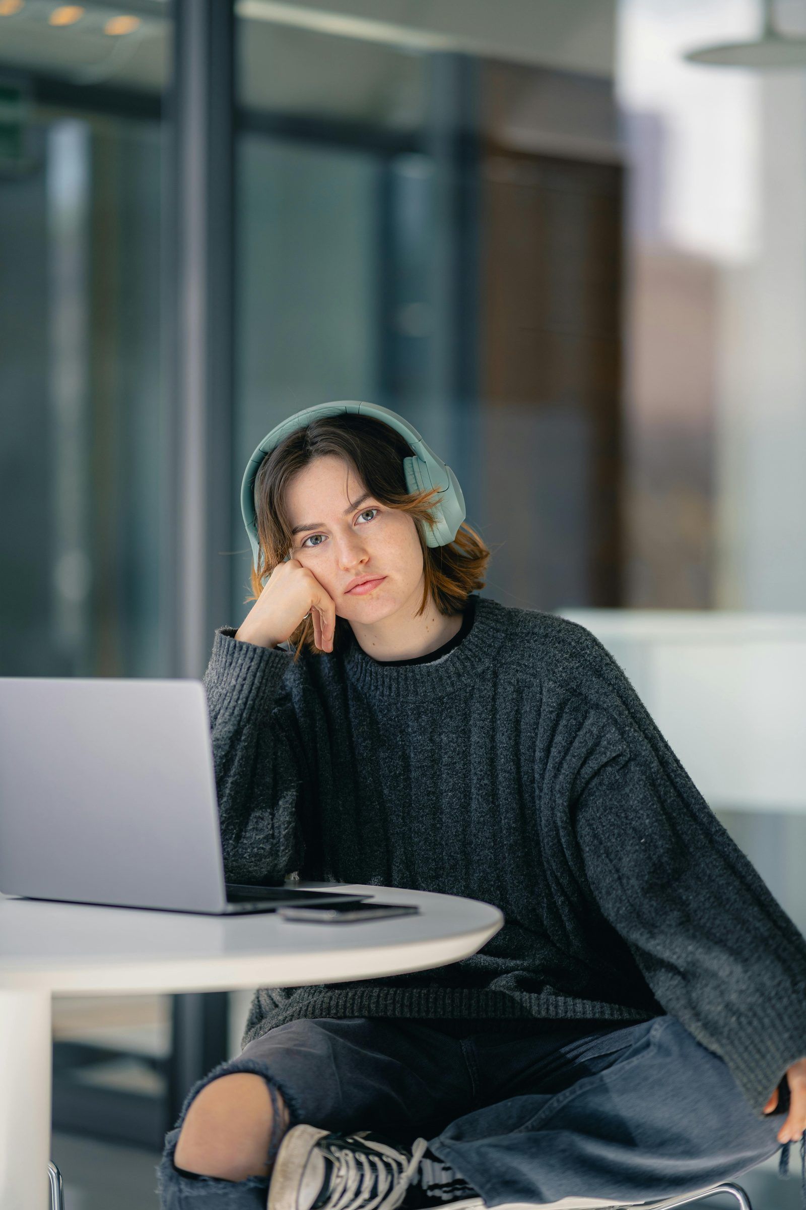 Vrouw met groene koptelefoon luistert achter laptop in modern kantoor